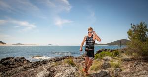 Triathlete running across the rocky foreshore at Fingal Bay