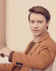 Calum Worthy, seated in a chair, turning to the camera