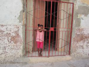 Young girl in Havana standing behind red bars