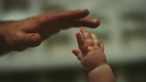 Photograph of an adult hand and an infant's hand about to touch.