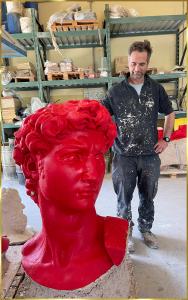 Foundry worker next to red wax David head that comes to his shoulders in height.
