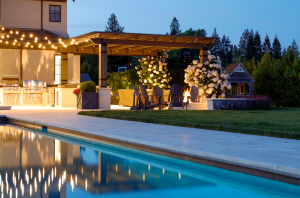 Nightscape backyard with pergola, firepit, outdoor kitchen and custom pool.